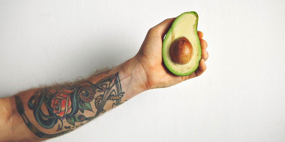 Man's tattooed arm holding an avocado